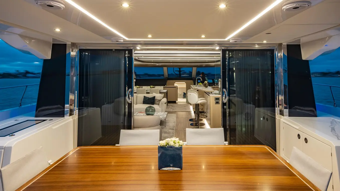 Modern yacht interior featuring a dining table, lounge area, and kitchen, with panoramic windows overlooking the water.